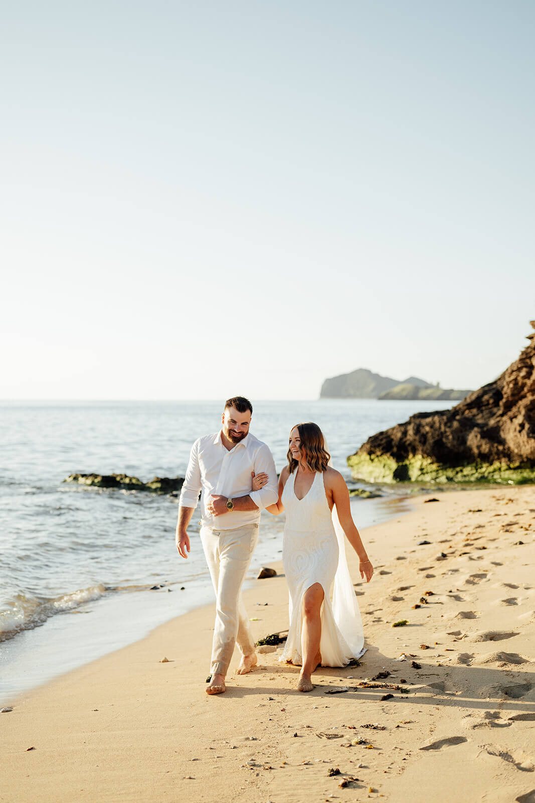 A couple walking hand in hand along a beach at the water&rsquo;s edge