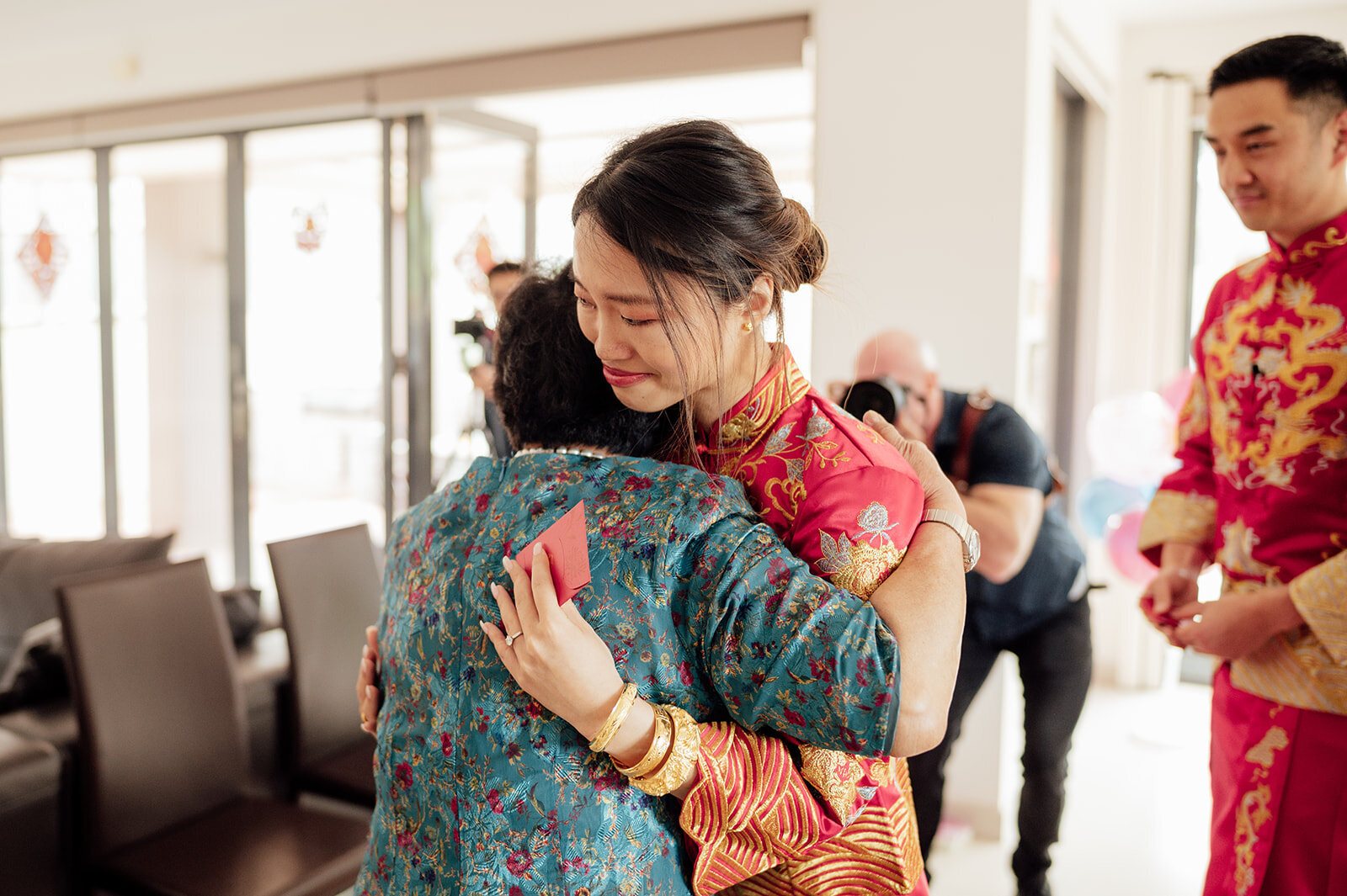 A bride in a red qipao hugging a family member while the groomsmen look on