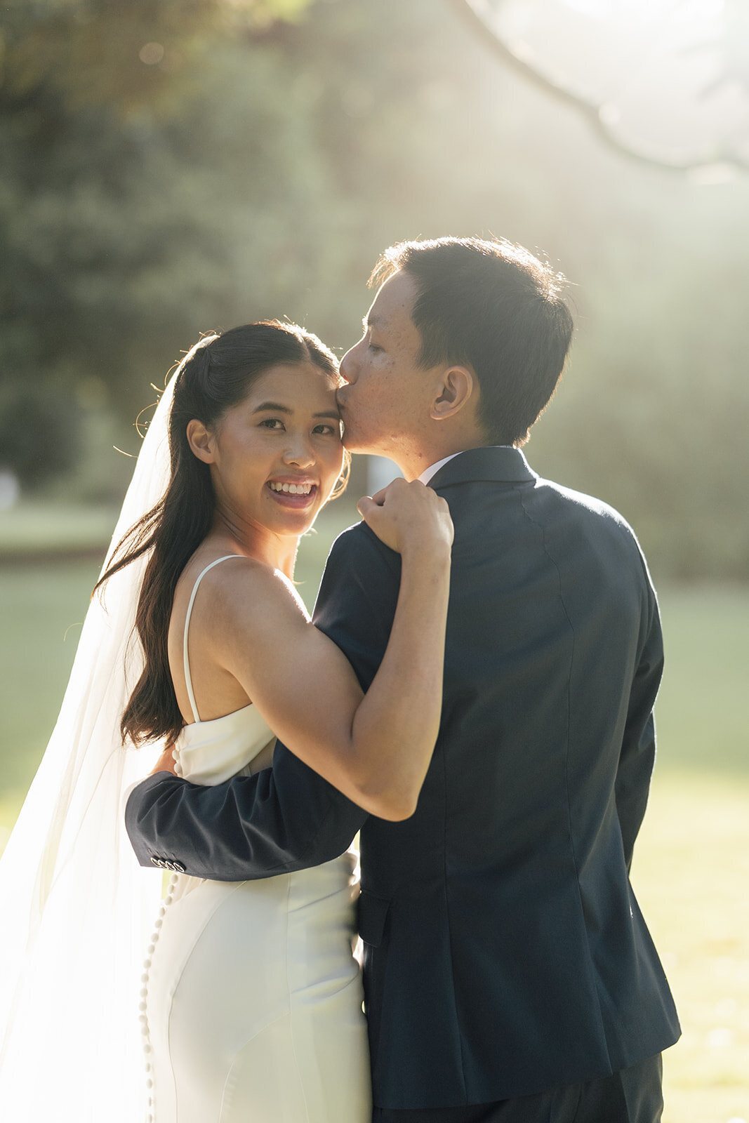 A groom kissing his bride on the cheek in golden late-afternoon light