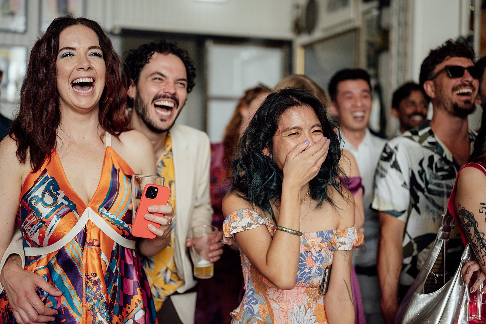 Wedding guests crying with laughter in a crowd, one woman covering her mouth