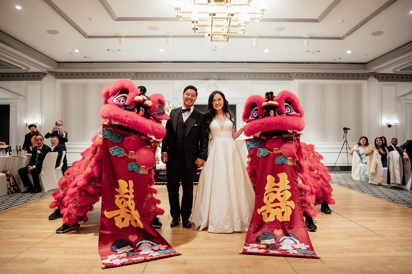Lion dancers in red and gold leaning over the couple&rsquo;s table at their reception