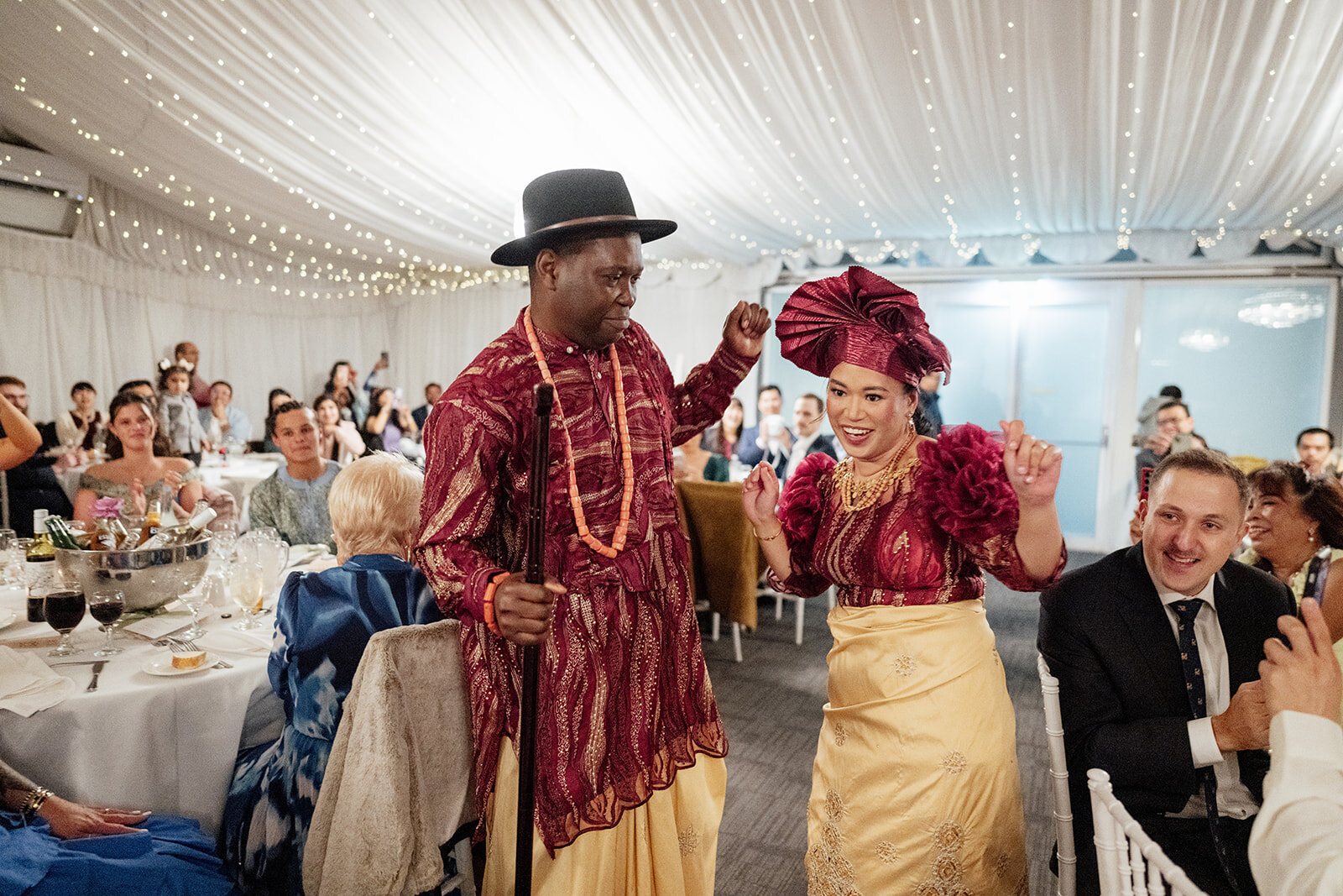 A couple in traditional dress dancing into their marquee reception as guests cheer