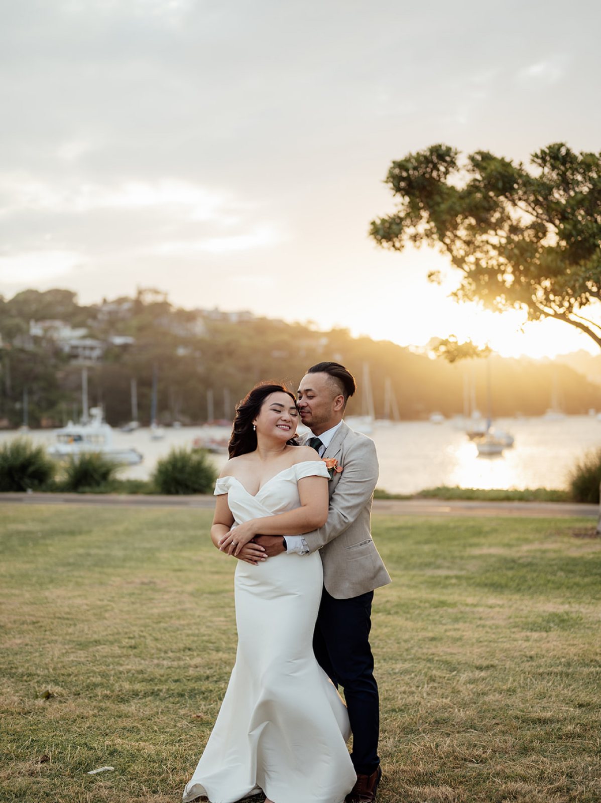 Thu and Jose embracing on a harbourside lawn at sunset